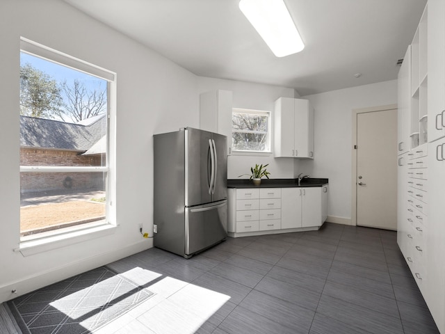 kitchen featuring baseboards, dark countertops, freestanding refrigerator, tile patterned flooring, and white cabinetry