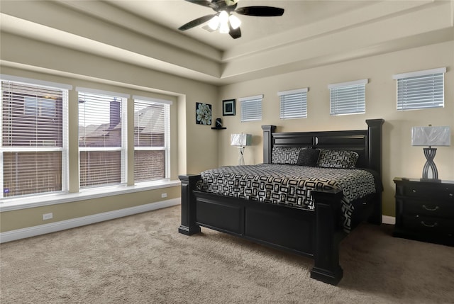 carpeted bedroom with a tray ceiling, a ceiling fan, and baseboards