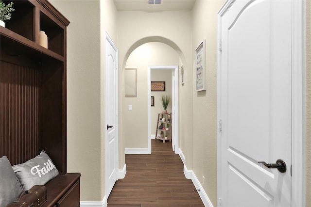 corridor with arched walkways, dark wood-style flooring, visible vents, and baseboards