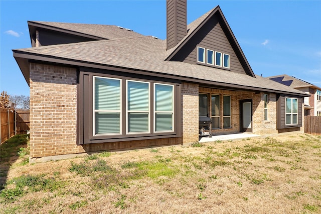 rear view of house featuring a chimney, brick siding, a lawn, and a fenced backyard