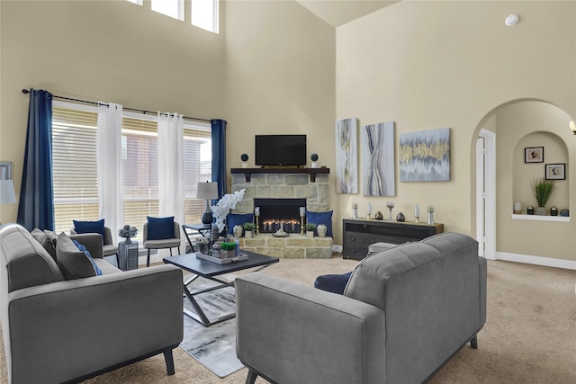 living room featuring arched walkways, a high ceiling, carpet flooring, a stone fireplace, and baseboards