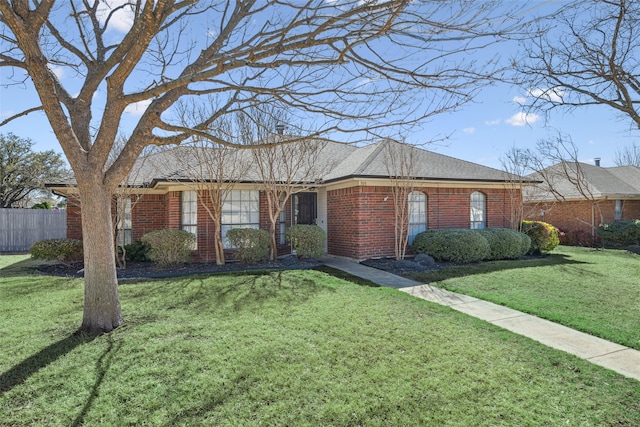 ranch-style home with brick siding, a front yard, fence, and a shingled roof