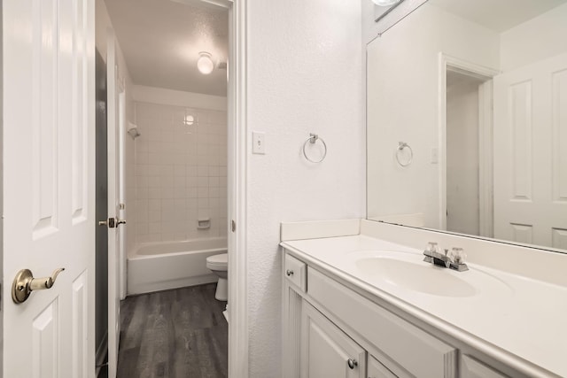 full bathroom with a textured wall, toilet, wood finished floors, vanity, and washtub / shower combination