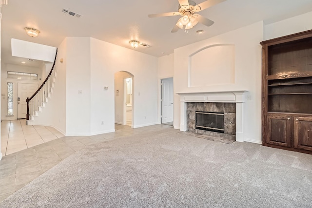 unfurnished living room with light tile patterned floors, light colored carpet, visible vents, stairway, and a tiled fireplace