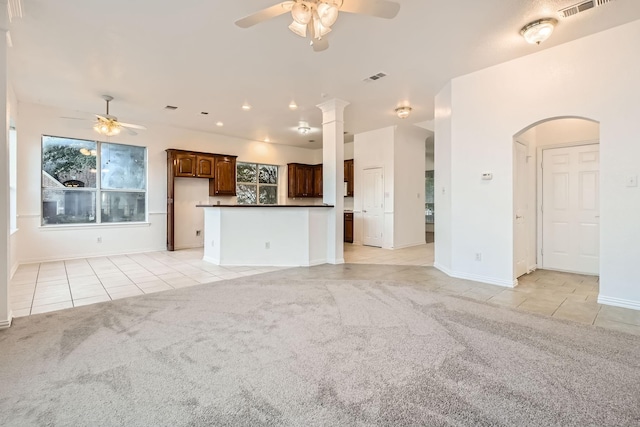 unfurnished living room featuring arched walkways, ceiling fan, light tile patterned floors, light colored carpet, and visible vents