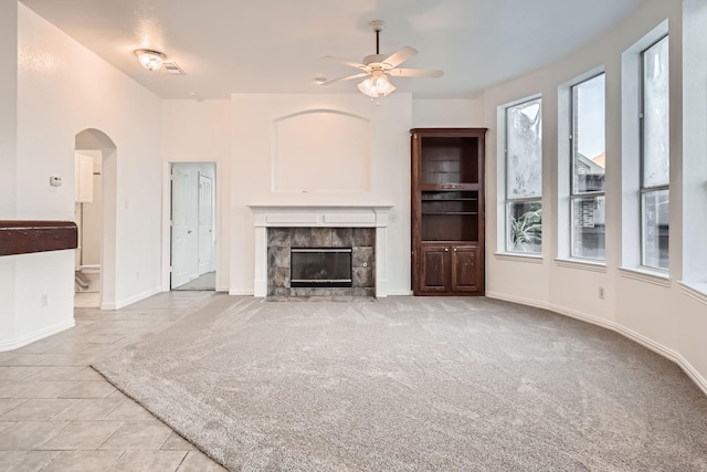 unfurnished living room with arched walkways, light carpet, a fireplace, a ceiling fan, and baseboards