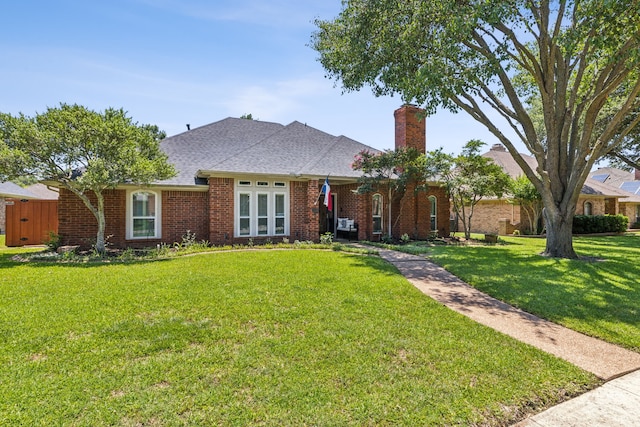 ranch-style home with a shingled roof, a front yard, a chimney, and brick siding