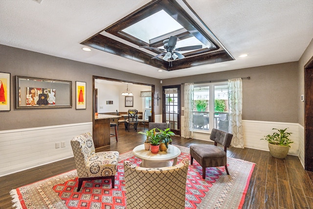 sitting room with dark wood-style floors, a tray ceiling, a wainscoted wall, and a skylight