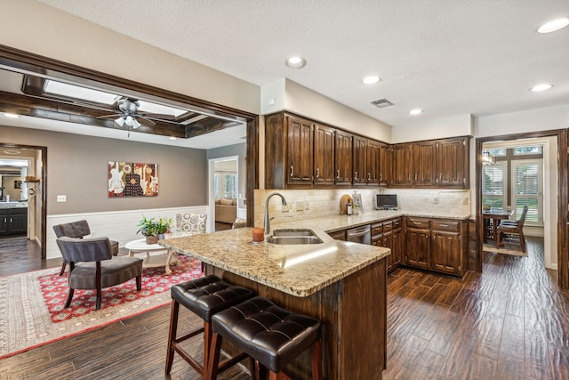 kitchen with visible vents, dark wood-style floors, a peninsula, light stone countertops, and a sink