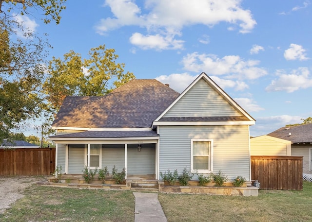 view of front of home with a shingled roof, covered porch, fence, and a front lawn