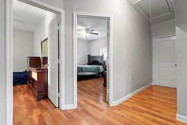 hallway with light wood finished floors, attic access, and baseboards