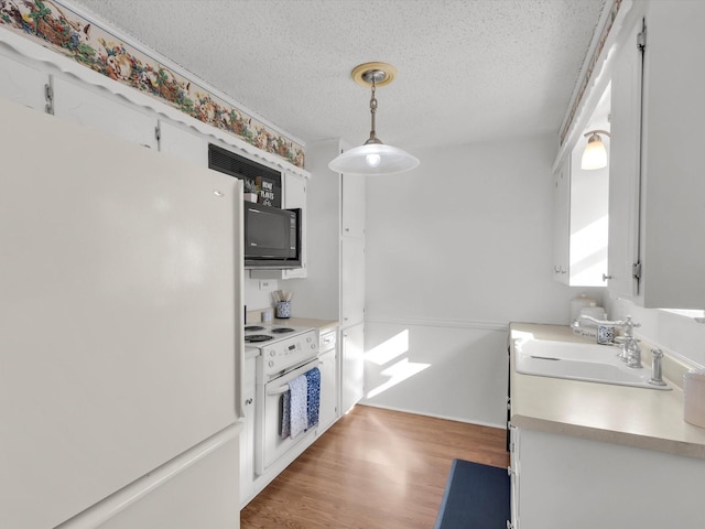 kitchen with freestanding refrigerator, white cabinets, wood finished floors, black microwave, and oven