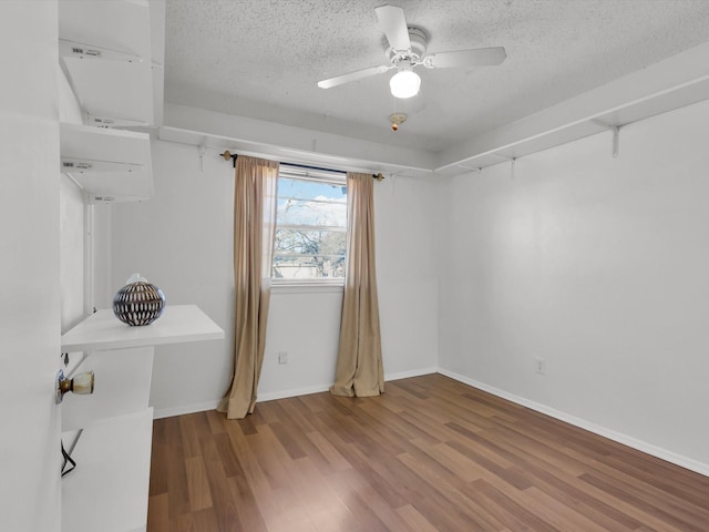 interior space with a ceiling fan, a textured ceiling, baseboards, and wood finished floors