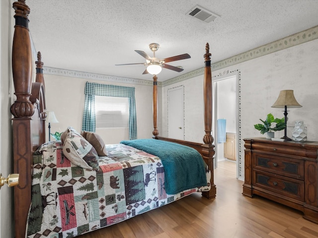 bedroom with a textured ceiling, wood finished floors, visible vents, and a ceiling fan