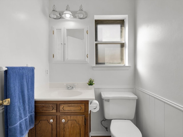 half bath featuring toilet, a wainscoted wall, and vanity