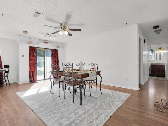 dining area featuring a textured ceiling, wood finished floors, visible vents, and a ceiling fan