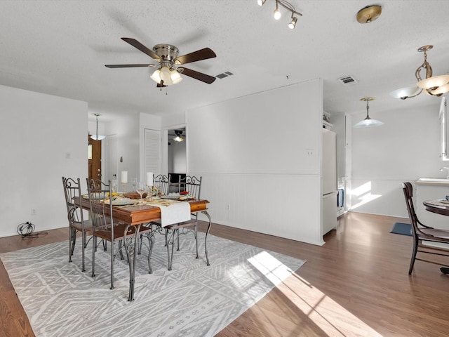 dining space featuring a ceiling fan, a textured ceiling, visible vents, and wood finished floors