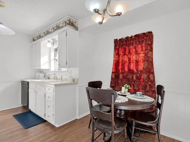 dining area with a textured ceiling, wainscoting, and light wood-type flooring