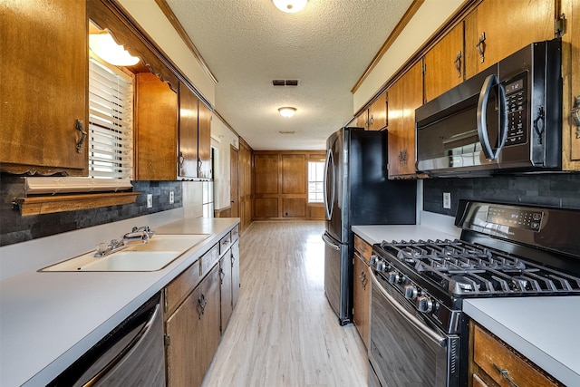 kitchen with a sink, gas range oven, light countertops, light wood-type flooring, and stainless steel dishwasher