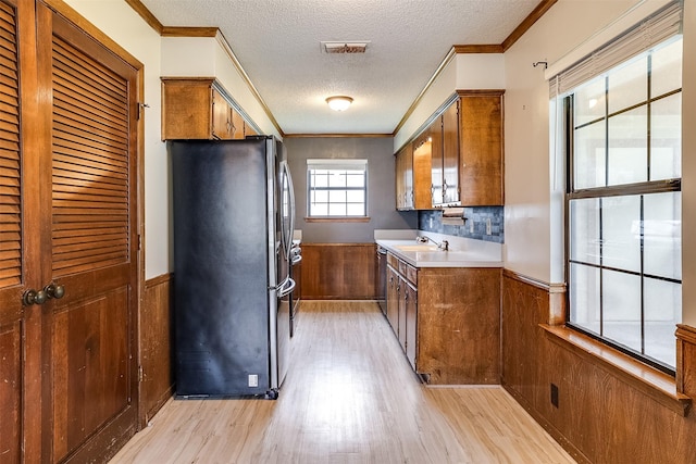 kitchen featuring a wainscoted wall, appliances with stainless steel finishes, brown cabinets, and ornamental molding