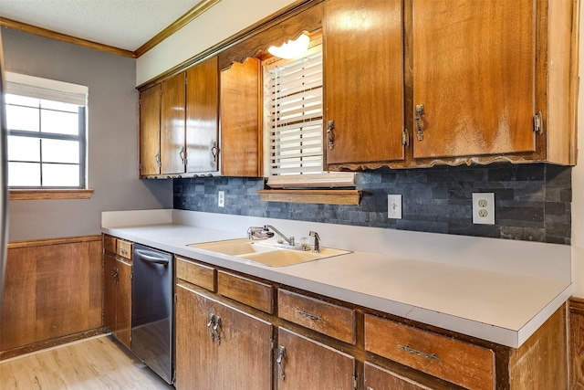 kitchen featuring crown molding, light wood finished floors, light countertops, a sink, and dishwasher