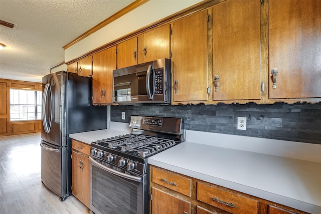 kitchen featuring light wood finished floors, brown cabinetry, stainless steel microwave, gas range oven, and light countertops