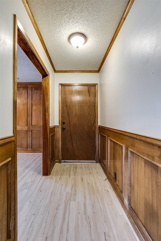 entryway featuring light wood-type flooring, a wainscoted wall, crown molding, and a textured ceiling