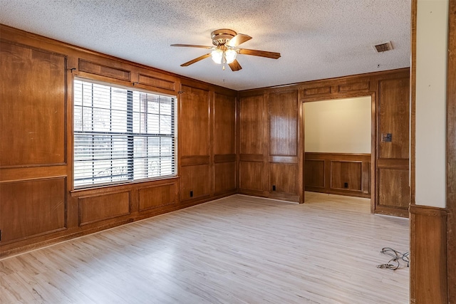 spare room with a textured ceiling, visible vents, light wood-type flooring, and a ceiling fan