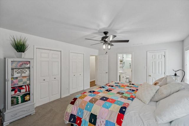 bedroom featuring two closets, visible vents, ensuite bathroom, a ceiling fan, and carpet flooring