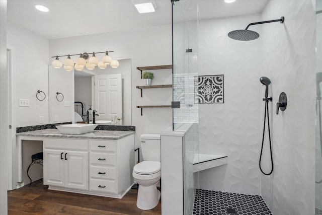 bathroom with a tile shower, vanity, toilet, and wood finished floors