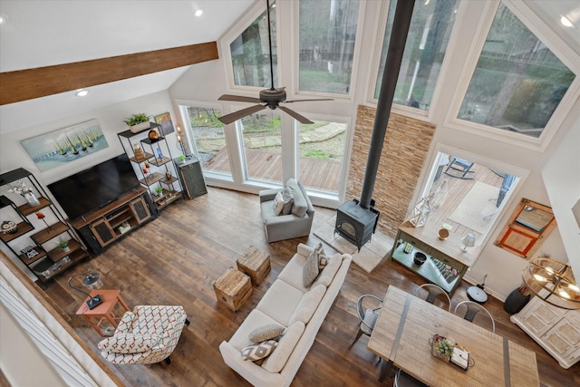 living room featuring baseboards, a ceiling fan, wood finished floors, a wood stove, and high vaulted ceiling