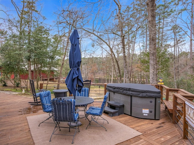 wooden deck featuring a hot tub, fence, outdoor dining area, and a wooded view