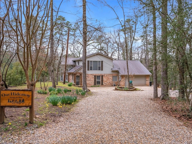 view of front of house featuring a garage, driveway, brick siding, and metal roof