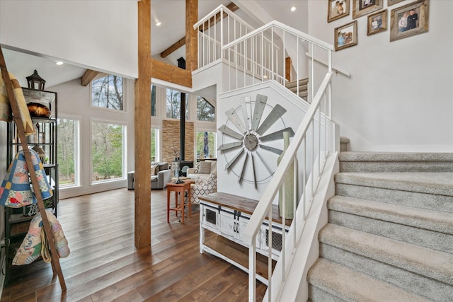 stairs with beam ceiling, recessed lighting, a wood stove, high vaulted ceiling, and hardwood / wood-style flooring