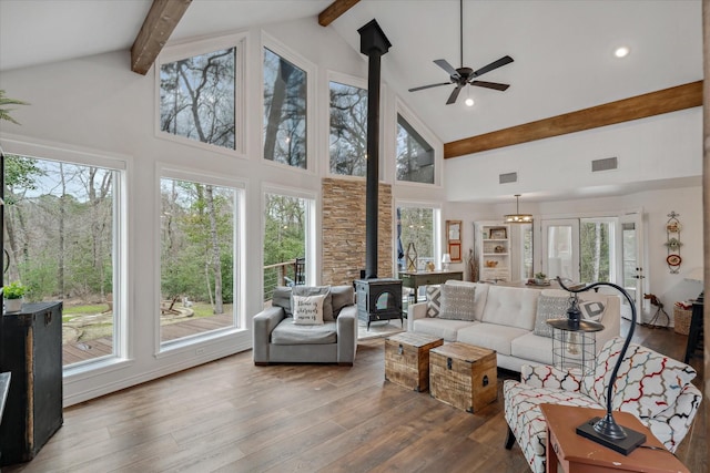 living area featuring visible vents, beamed ceiling, wood finished floors, and a wood stove