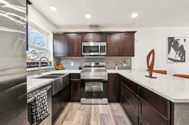 kitchen with stainless steel appliances, tasteful backsplash, a peninsula, and dark brown cabinetry