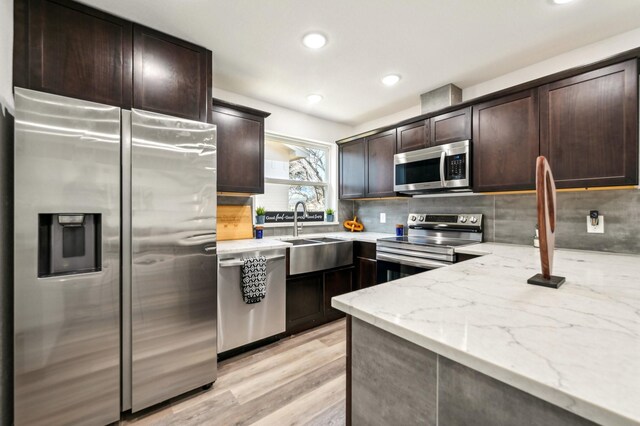 kitchen featuring stainless steel appliances, light stone counters, a sink, and dark brown cabinetry