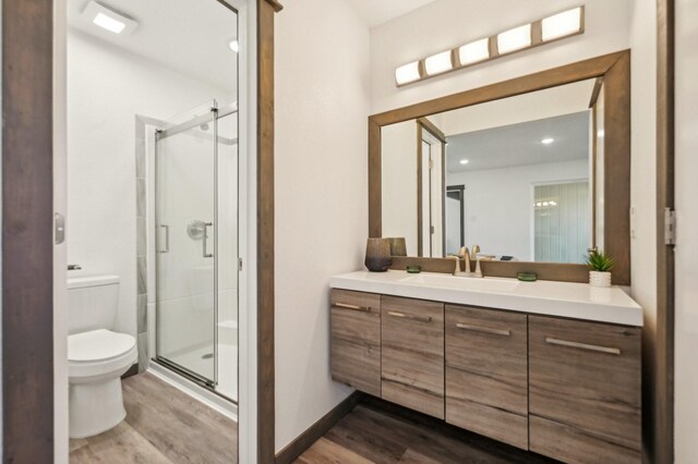 bathroom with baseboards, toilet, wood finished floors, vanity, and a shower stall