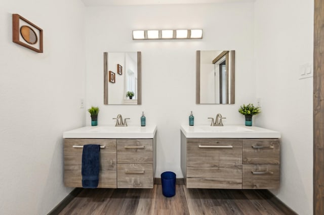 full bath featuring two vanities, a sink, baseboards, and wood finished floors