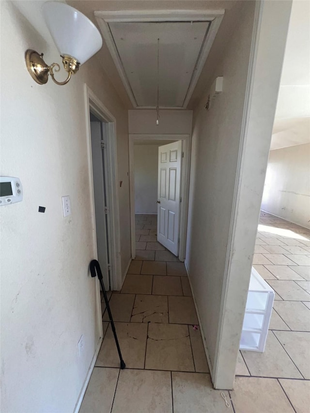 hall with light tile patterned floors, attic access, and baseboards