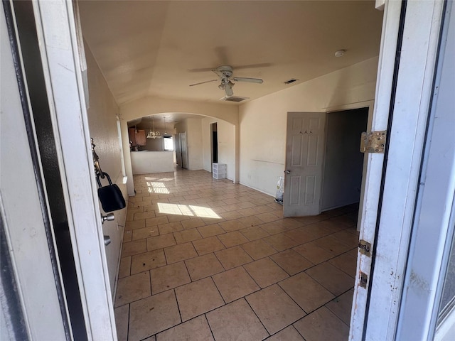 tiled empty room with visible vents, arched walkways, vaulted ceiling, and a ceiling fan