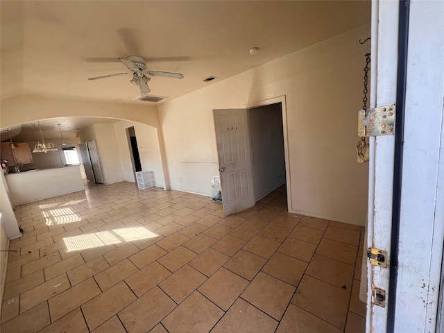 spare room featuring light tile patterned floors, ceiling fan, arched walkways, visible vents, and vaulted ceiling