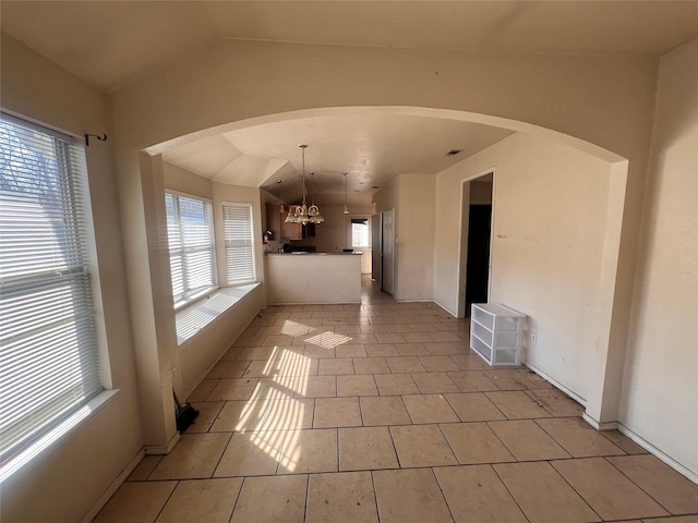 interior space with arched walkways, vaulted ceiling, an inviting chandelier, and light tile patterned floors