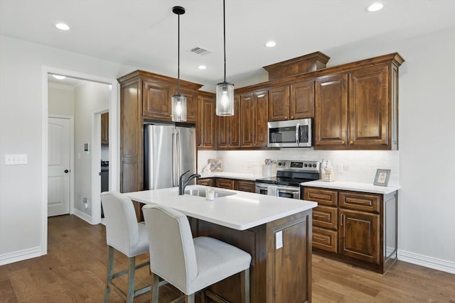 kitchen featuring visible vents, decorative backsplash, wood finished floors, stainless steel appliances, and a sink