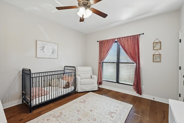 bedroom featuring dark wood-style floors, ceiling fan, a nursery area, and baseboards