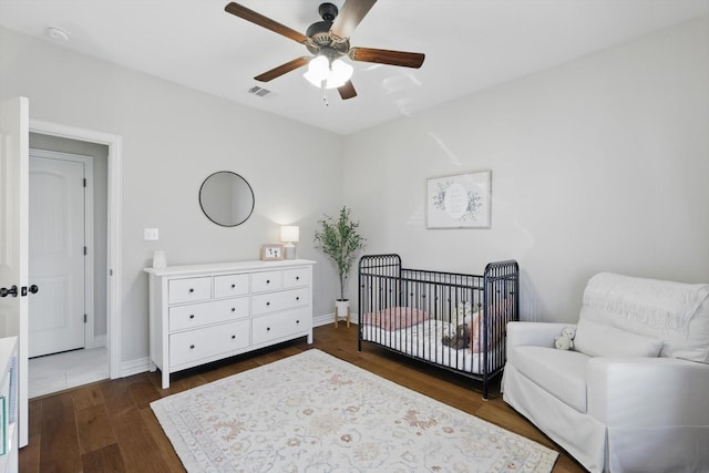 bedroom with visible vents, baseboards, a ceiling fan, a nursery area, and dark wood finished floors