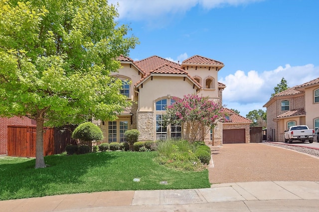 mediterranean / spanish home featuring driveway, stone siding, fence, and a front lawn