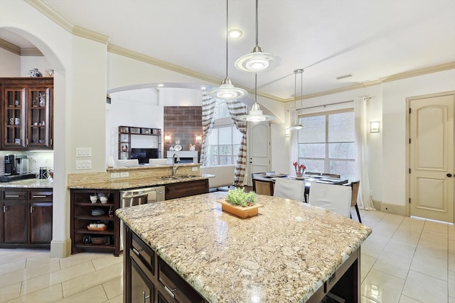 kitchen featuring light tile patterned floors, a center island, dark brown cabinets, crown molding, and a sink