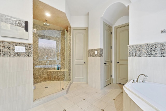 bathroom with tile walls, a wainscoted wall, tile patterned flooring, a shower stall, and a bath