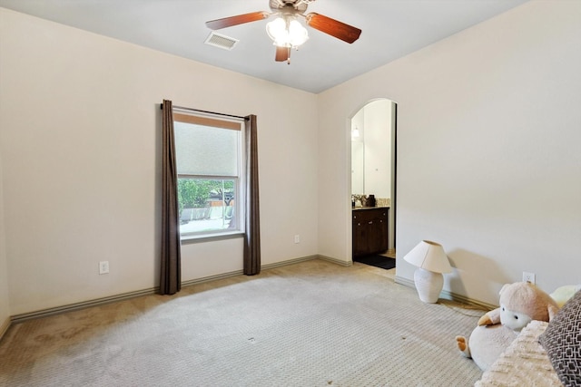 unfurnished bedroom with light carpet, visible vents, arched walkways, a ceiling fan, and connected bathroom